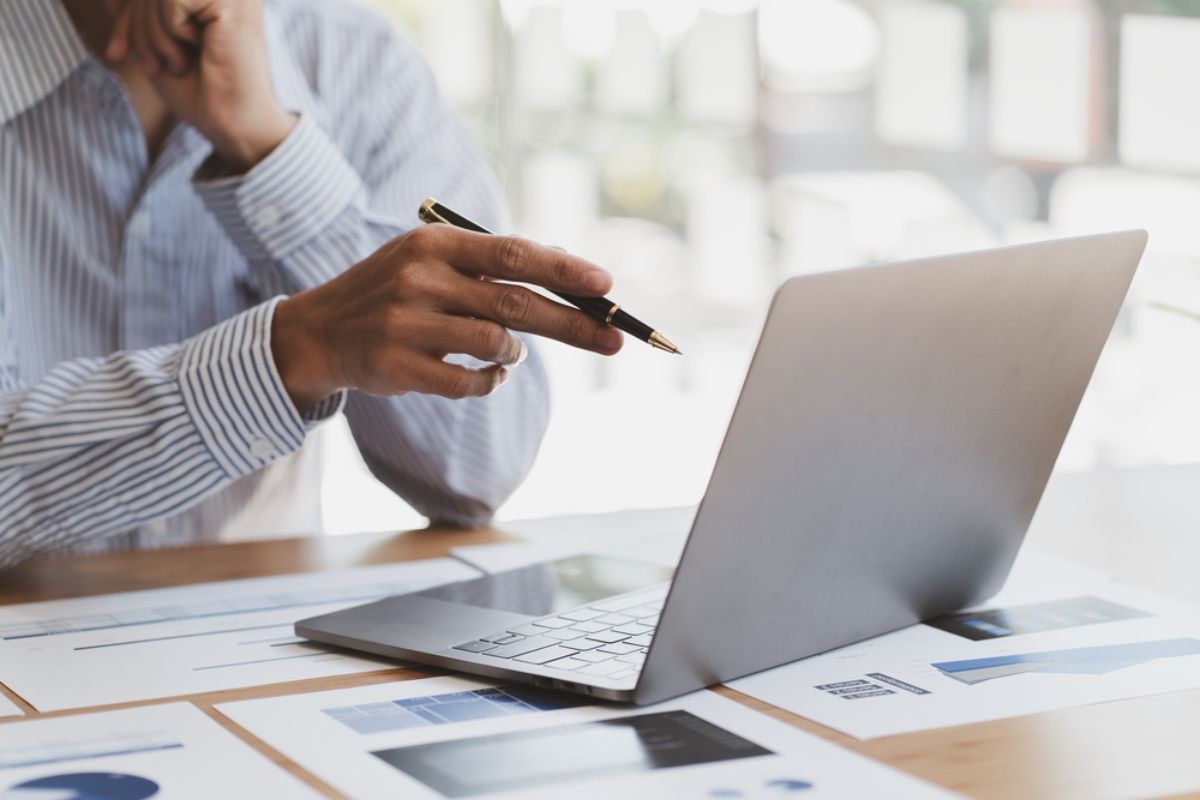 a person with a pen pointing at a laptop